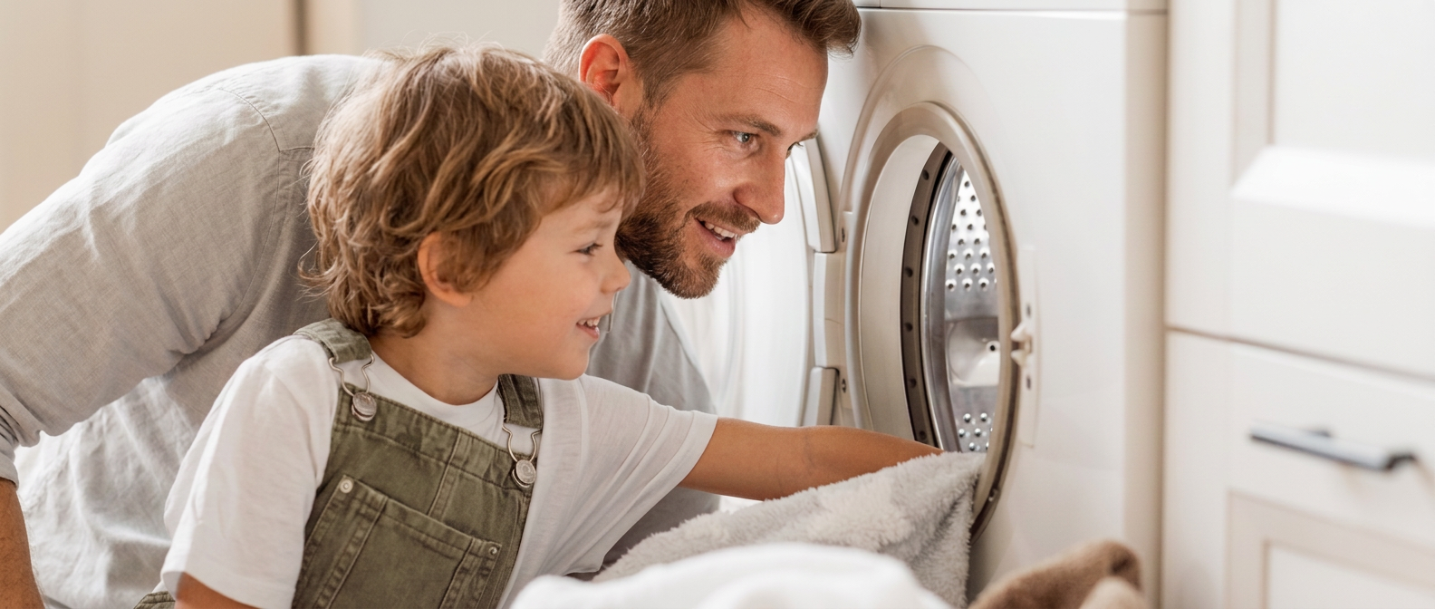 Father and child loading towels into a dryer at home